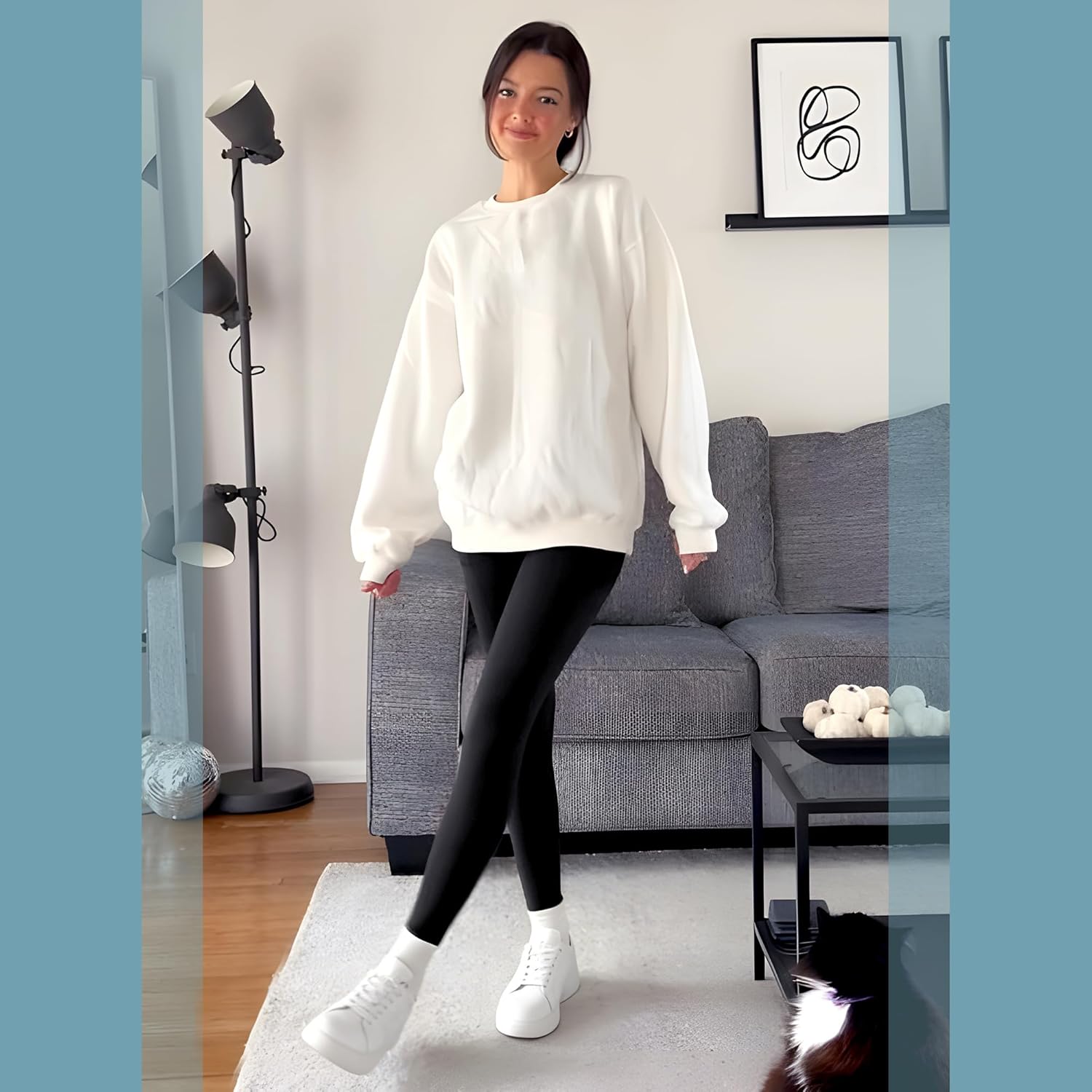 Woman wearing a white oversized sweatshirt and black leggings in a living room.